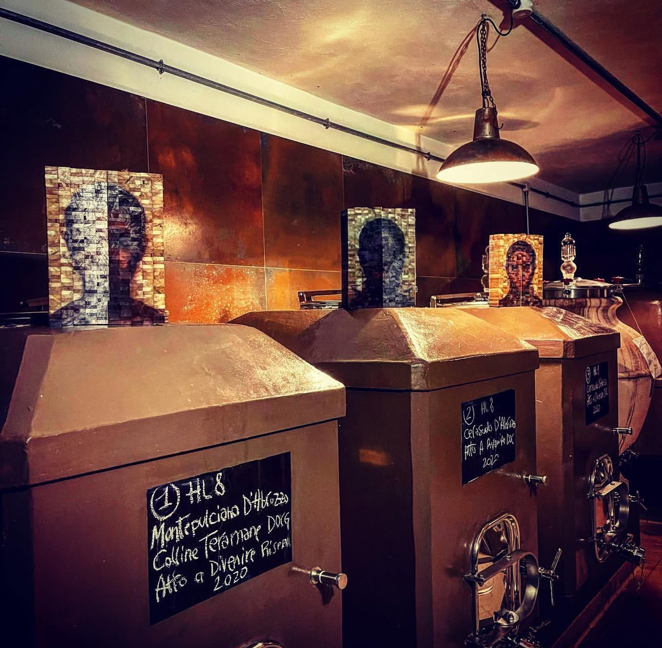 Concrete fermentation tanks in the Bossanova cellar, marked with chalk labels and framed by portraits